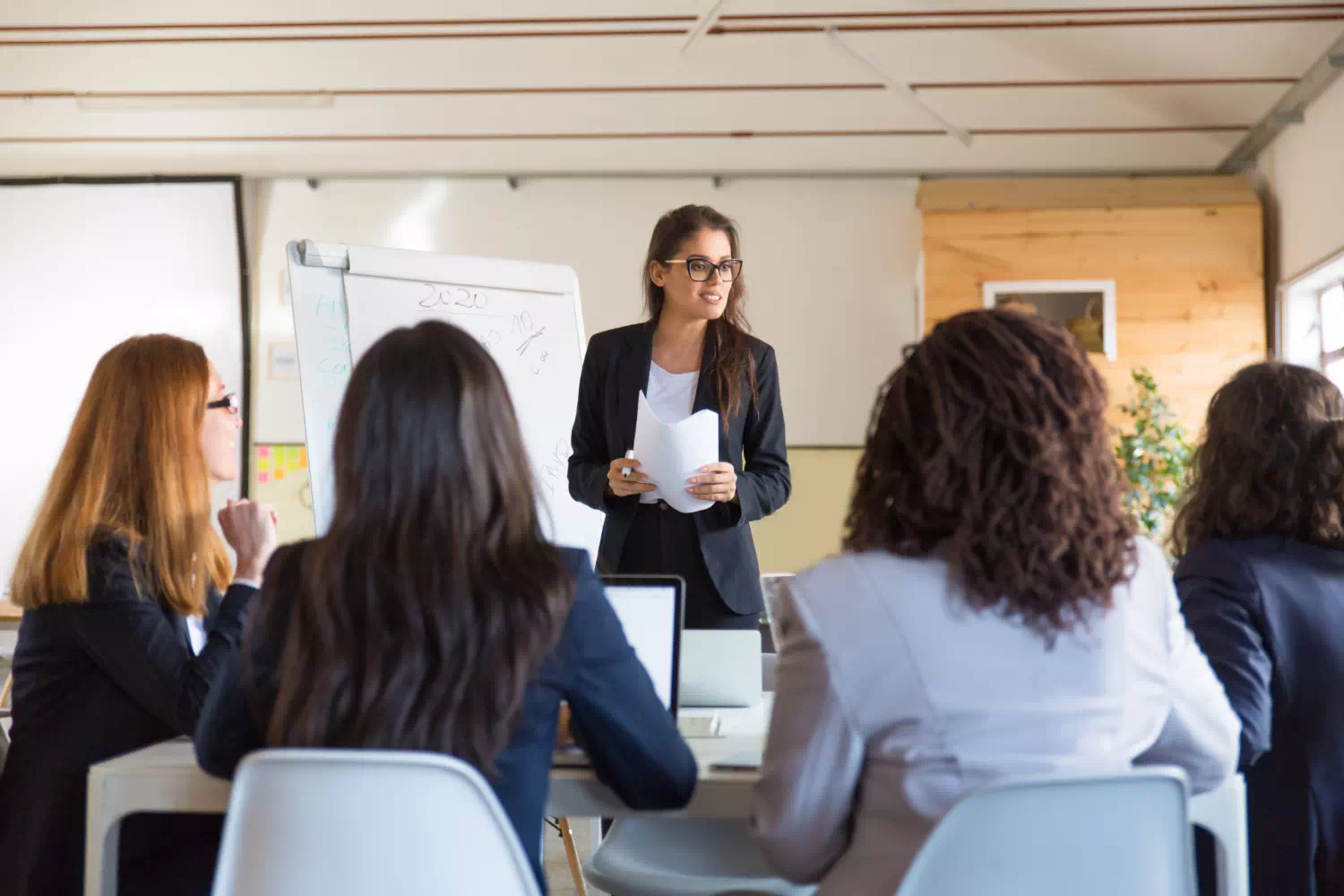 Manager donna autorevole si rivolge a dipendenti durante meeting, una delle competenze manageriali più importanti